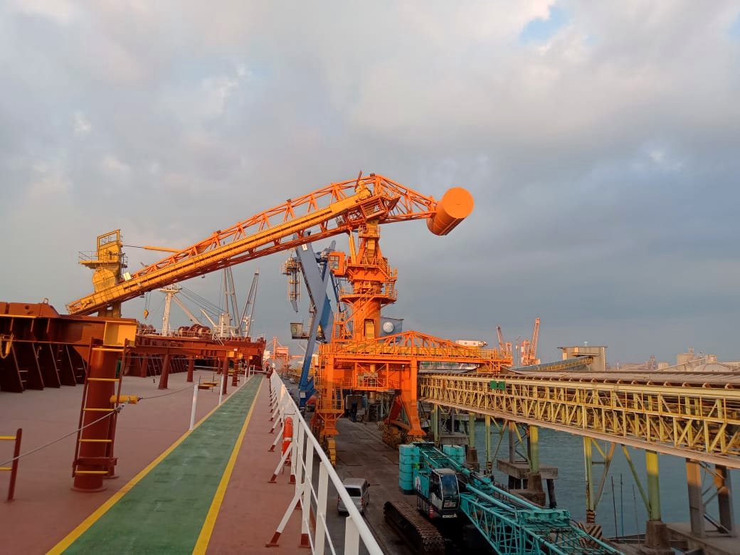 Continuous ship unloader berwarna oranye beroperasi di atas geladak kapal curah saat matahari terbenam di Pelabuhan Cigading